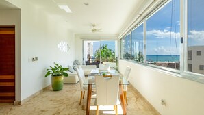 A modern dining area with a glass table and chairs, a potted plant, and a view of the ocean. - Beachfront Condo w/ Large Balcony and Ocean Views near Downtown Playa Del Carmen (Playa del Carmen)
