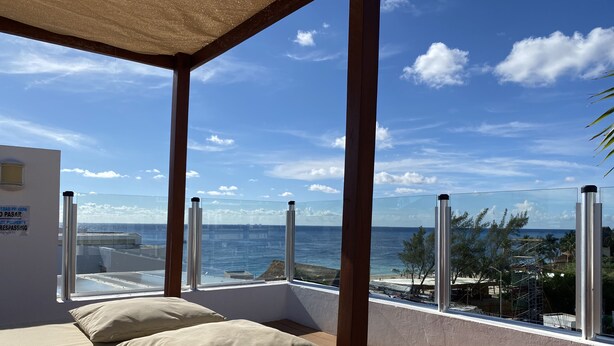 A balcony with a view of the sea, a bed with beige pillows, and a sign indicating private property. - Beachfront Condo w/ Large Balcony and Ocean Views near Downtown Playa Del Carmen (Playa del Carmen)