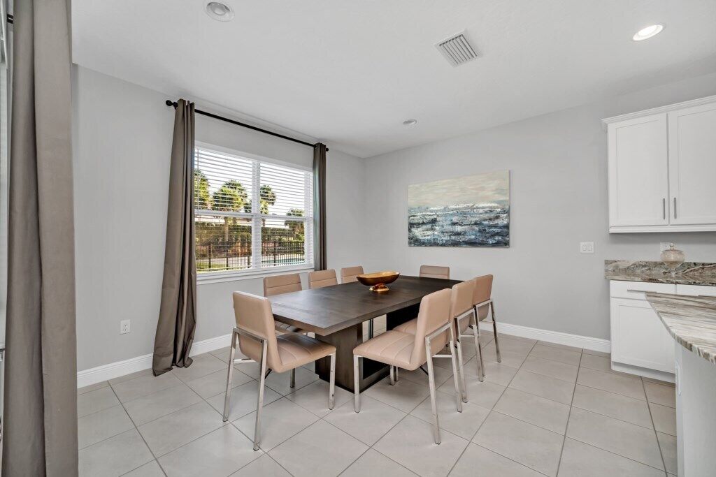 Uma área de refeições com uma mesa retangular e seis cadeiras, uma janela com persianas e um quadro na parede.