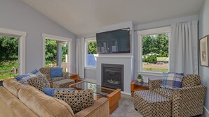 A living room with a fireplace, patterned sofas, and a television. - A modern cozy cottage in your own wooded backyard located mid Vancouver Island. (Qualicum Beach)