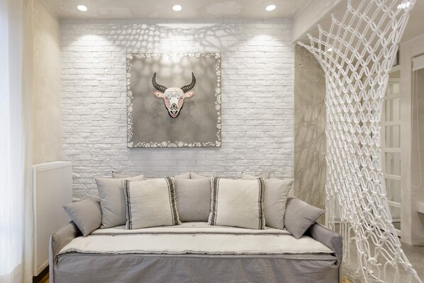 A bedroom with a white brick wall, a decorative bull head artwork, a bed with grey bedding, and a white macramé wall hanging. - Stylish, Quiet & Relaxing, a Hidden Gem near the Acropolis (Athina)