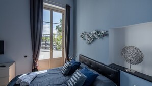 Ein Schlafzimmer mit Bett, Nachttisch, Wandlampe und Blick ins Freie durch ein Fenster.