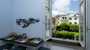Ein Zimmer mit Esstisch für zwei Personen, einem dekorativen Wandbild und Blick auf eine Wohngegend mit Gebäuden und Grünflächen.