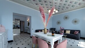 Ein modernes Wohnzimmer mit einem weißen Esstisch, rosafarbenen Stühlen, einem dunklen Sofa und Wanddekoration.