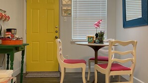 Comedor con puerta amarilla, sillas de madera con cojines rojos, una mesa redonda y una lámpara colgante.