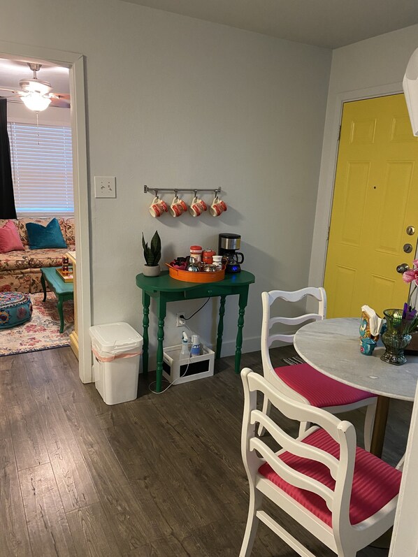 Una cocina compacta con zona de comedor, que incluye una mesa verde, sillas blancas y una puerta amarilla.