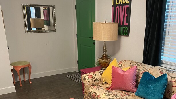 Una sala de estar con un sofá floral, una mesa de centro verde y un espejo en la pared.