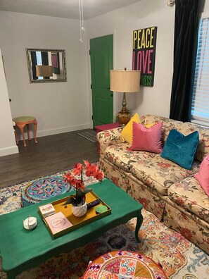 Una sala de estar con un sofá floral, una mesa de centro verde y un espejo en la pared.