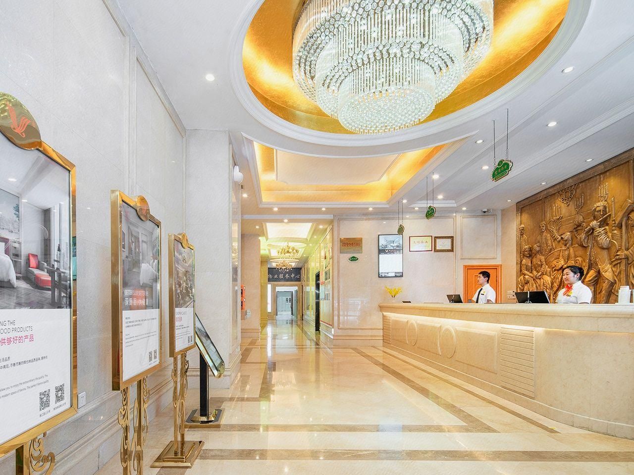 A hotel reception area with a chandelier, reception desk, and framed pictures on the wall.