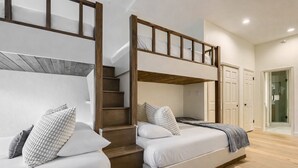 Une chambre d’hôtel moderne avec un escalier en bois reliant deux lits, un petit balcon et une porte donnant sur une salle de bain.