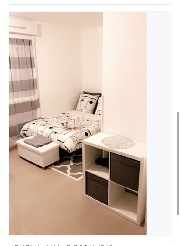 A bedroom with a bed, a bedside table, a small seating area, and a storage unit.