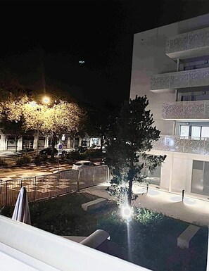 A nighttime view of a courtyard with a tree, a fence, and a building with balconies.