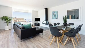 A modern living room with a black sofa, glass dining table, and chairs, a TV, and a large window with a view. - Home2Book Design Asian Sabina, Heated Pool & View (El Sauzal)
