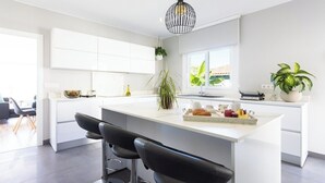 A modern kitchen with a central island, white cabinetry, and a hanging light fixture. - Home2Book Design Asian Sabina, Heated Pool & View (El Sauzal)