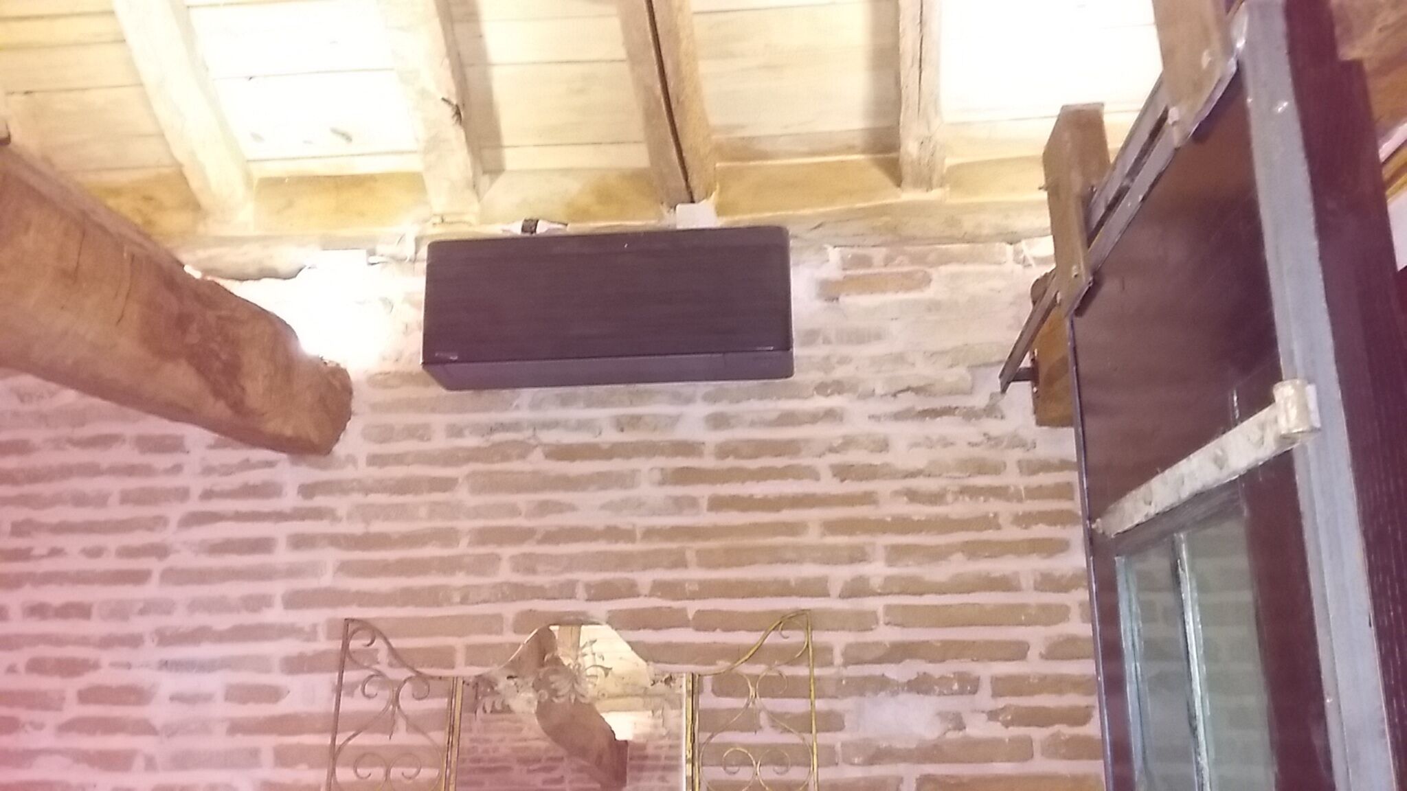 Quarto com parede de tijolos, teto de madeira e uma janela.