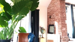 Un salon avec une cheminée en briques, une grande plante verte, un canapé en cuir et un luminaire suspendu.