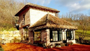 Une maison traditionnelle en briques, avec un toit en tuiles, de grandes fenêtres et un mur en pierre.