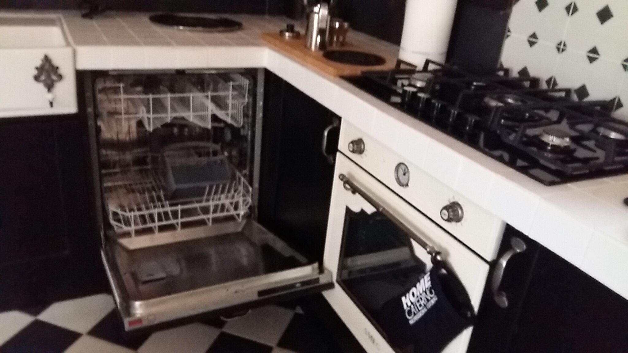 En åben ovn med en opvaskestativ indeni, en komfur med betjeningsknapper, og en køkkenbordplade.