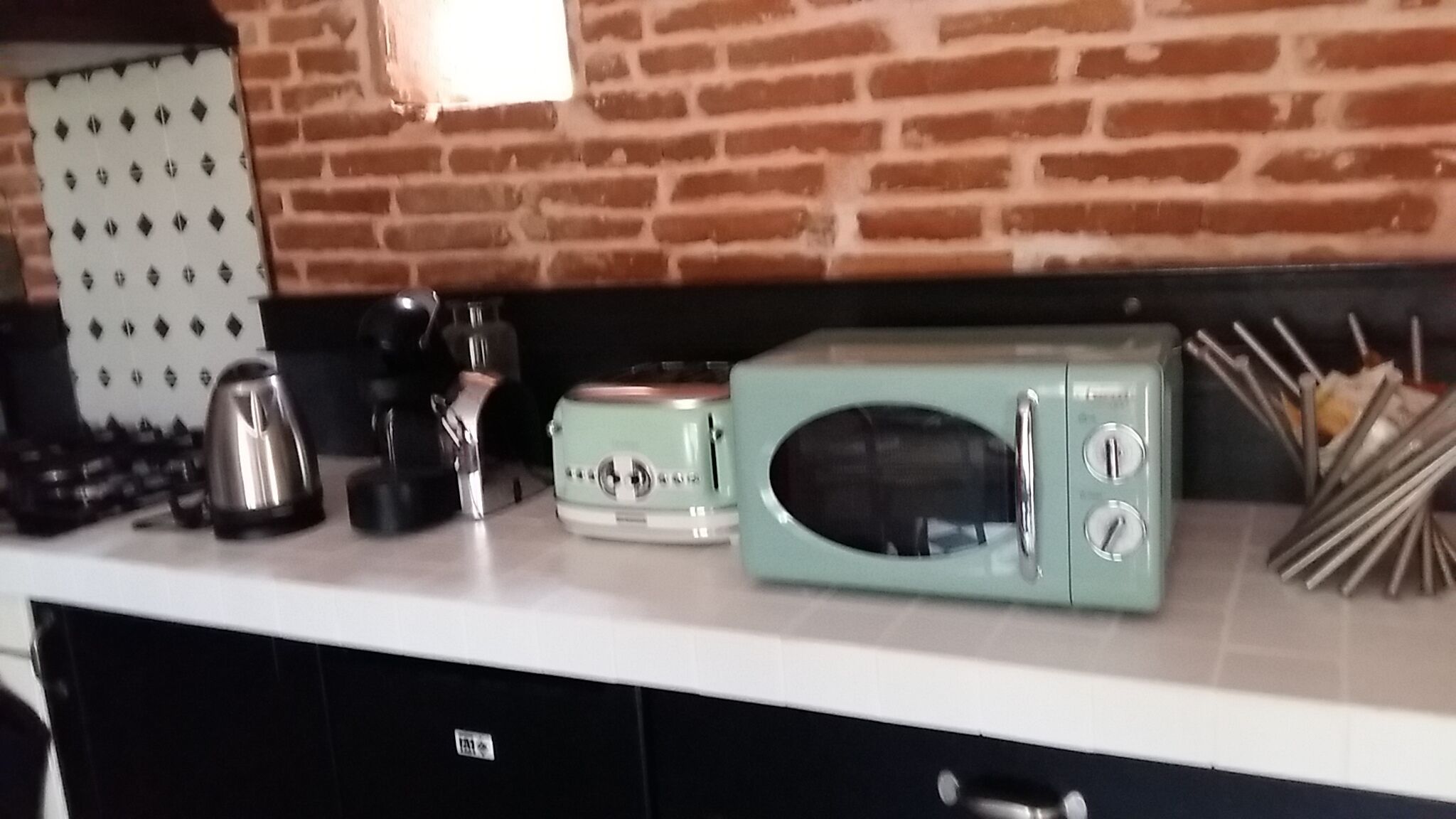A kitchen with a brick wall, a white countertop, a vintage-style toaster, a kettle, and a knife block.