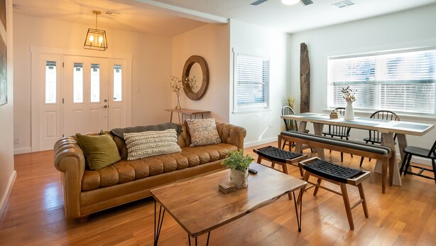 A living room with a brown leather sofa, a wooden coffee table, and a dining area with a wooden table and chairs. - Home in the Historic Coronado District 2bed,1 bath (Phoenix)