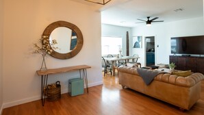 A modern living room with a wooden floor, a round mirror, a sofa, a dining area, and a ceiling fan. - Home in the Historic Coronado District 2bed,1 bath (Phoenix)