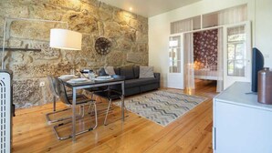 Una sala de estar moderna con una pared de piedra, un sofá, una mesa de comedor con sillas y un ventanal con cortinas.