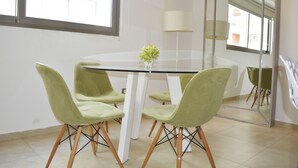 A dining area with a glass table surrounded by four green chairs, a vase with flowers, and a large mirror reflecting the room. - Menesse 25.26 (Playa del Carmen)