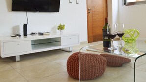 A modern living room with a flat-screen TV, a white entertainment unit, a glass coffee table, two knitted poufs, a wine bottle, and two wine glasses. - Menesse 25.26 (Playa del Carmen)
