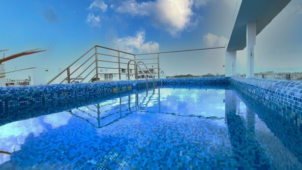 A rooftop swimming pool with a blue mosaic design, surrounded by a metal railing and a clear sky. - Menesse 25.26 (Playa del Carmen)