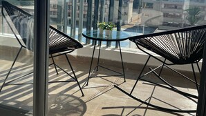 A balcony with two black chairs and a glass table, overlooking a cityscape with buildings and a clear sky. - Cozy and beautiful apartment 2 steps from la corniche (Dar-el-Beida)