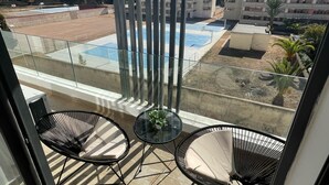 A balcony with two chairs, a small table, and a view of a swimming pool and buildings. - Cozy and beautiful apartment 2 steps from la corniche (Dar-el-Beida)