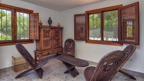 Une pièce comprenant un meuble en bois, deux chaises, une petite table et une fenêtre avec des volets en bois.