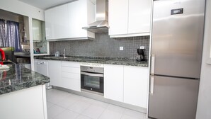 A modern kitchen with white cabinets, a stainless steel refrigerator, a built-in oven, and a coffee maker.