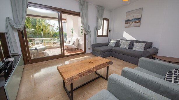 A modern living room with a grey sofa, a wooden coffee table, and a sliding glass door leading to a patio area.