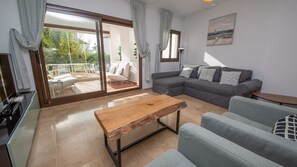 Un salon moderne avec un canapé gris, une table basse en bois et une porte-fenêtre coulissante donnant sur un espace patio.