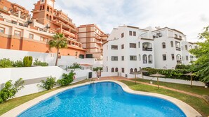 A swimming pool surrounded by a white building with balconies and a red building in the background.