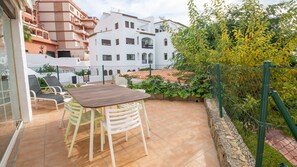 Un patio con una mesa y sillas de madera, rodeado por un muro de piedra y follaje.