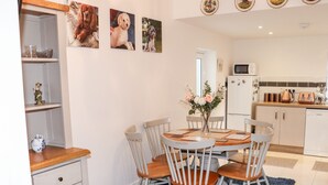 A dining area with a round table, four chairs, a vase with flowers, and a black furry rug. - Lane Cottage (Ballycullane)