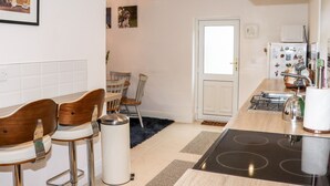 A modern kitchen with a built-in stove, white cabinets, and a dining area with wooden chairs. - Lane Cottage (Ballycullane)
