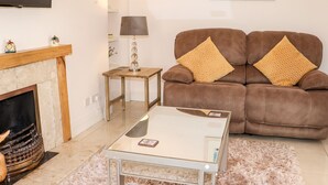 A living room with a sofa, a glass coffee table, a fireplace, a television, and a framed picture on the wall. - Lane Cottage (Ballycullane)