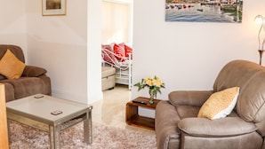 A living room with a sofa, armchair, and coffee table. There is a painting on the wall and a vase with flowers on a side table. - Lane Cottage (Ballycullane)