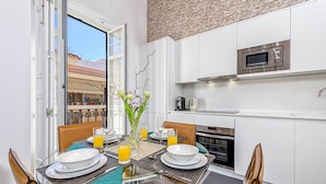 A modern kitchen with white cabinets, a microwave, and a stove. There is a dining table with chairs and a vase of flowers.