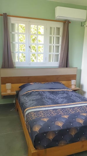 Quarto com cama, mesa de cabeceira, janela com cortinas e ar condicionado.