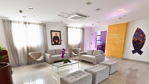 Un lobby moderno de hotel con área de descanso, una mesa de centro de vidrio y una gran pared decorada con arte geométrico.