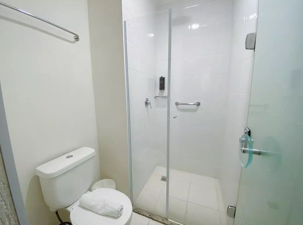 Un baño con inodoro, ducha con mampara de vidrio y puerta de cristal.