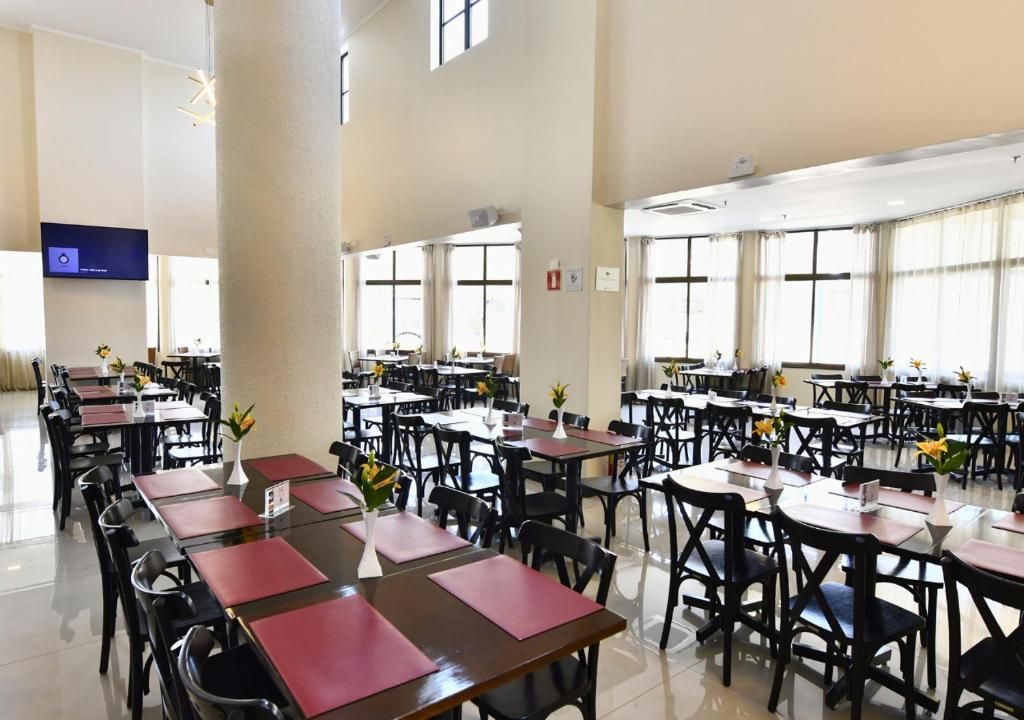 Uma sala de jantar ampla, com várias mesas e cadeiras, janelas grandes e uma TV de tela plana na parede.
