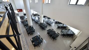A spacious dining area with multiple tables and chairs, high ceilings, and large windows allowing natural light.