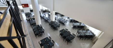 Un amplio comedor con varias mesas y sillas, techos altos y ventanas grandes que dejan entrar luz natural.