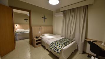 Habitación de hotel con cama, mesita de noche, escritorio, silla y equipo de aire acondicionado.