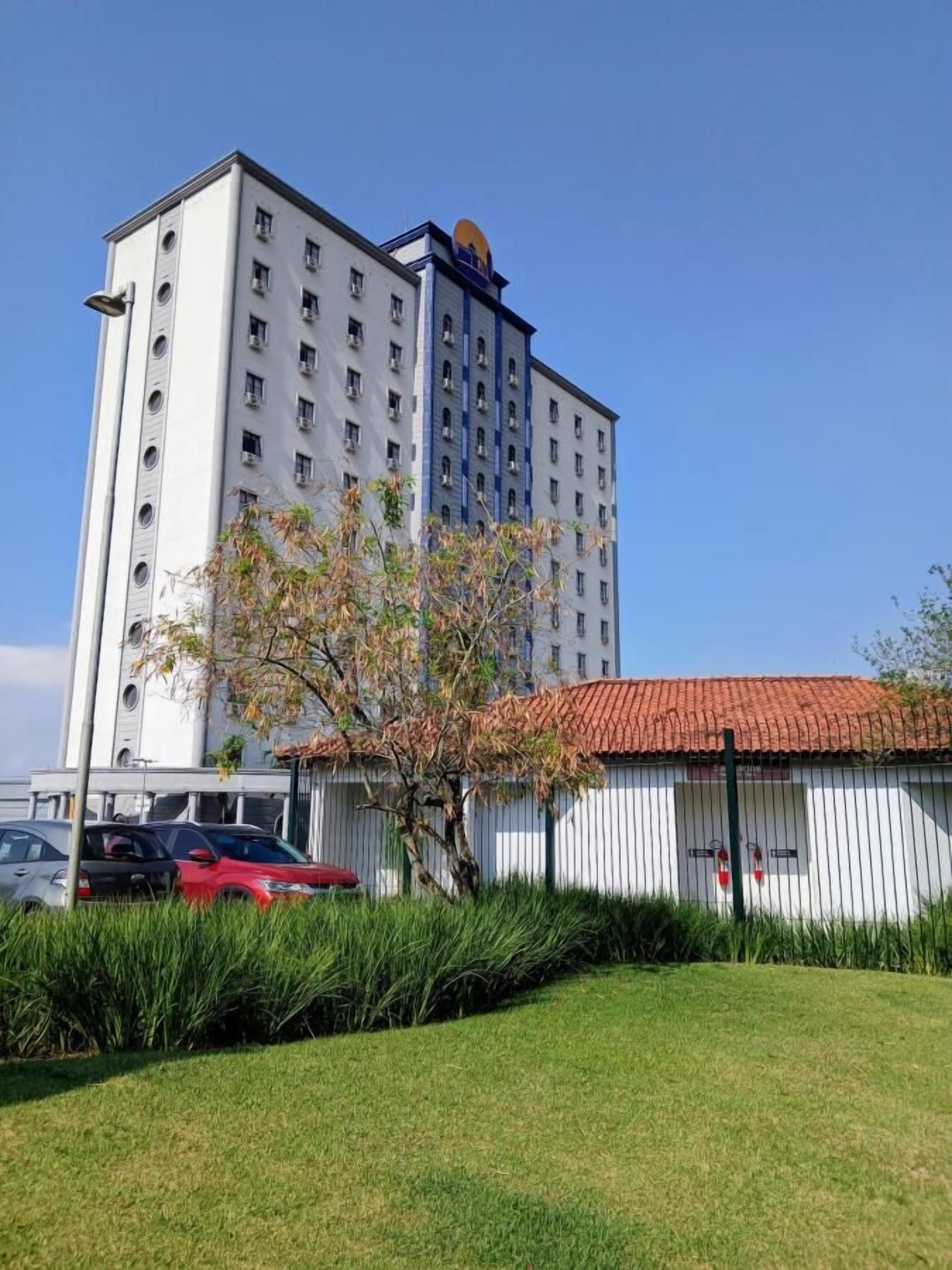 Un edificio de varios pisos con techo plano y una estructura más pequeña con tejado de tejas rojas al frente.